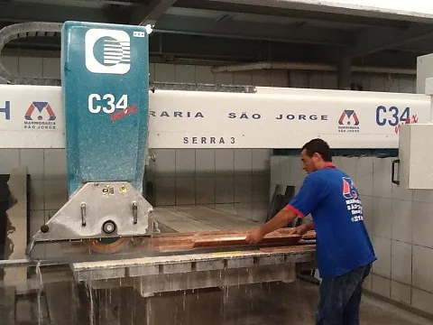 Operador cortando uma chapa na serra ponte, com o nome da empresa na máquina