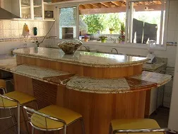 Área gourmet com ilha de granito claro sobre marcenaria de madeira