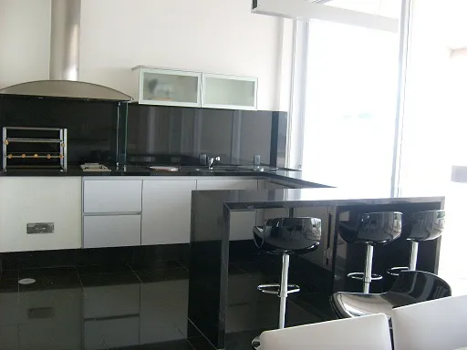 Cozinha com bancada e ilha em granito preto, banquetas e armários brancos