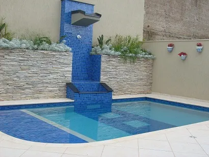 Área de piscina com cascata revestida de pastilha azul e bordas em mármore claro