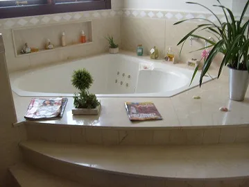 Banheira de canto com deck em mármore bege e nicho de plantas